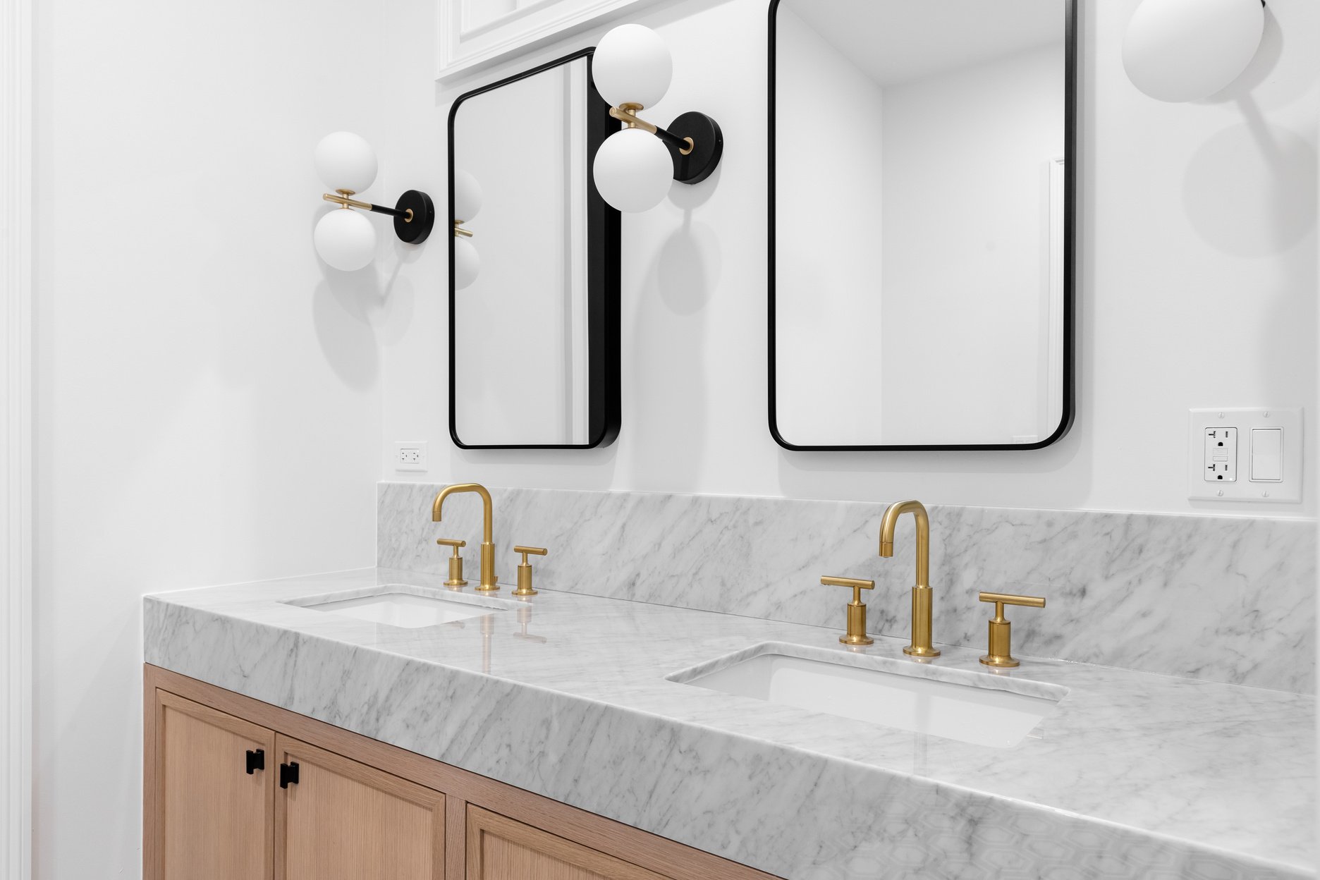 A bathroom with a white oak cabinet, marble countertop, and black and gold sconces.